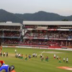 Sitanshu Kotak, the renowned cricketer, standing confidently in a bustling cricket stadium.